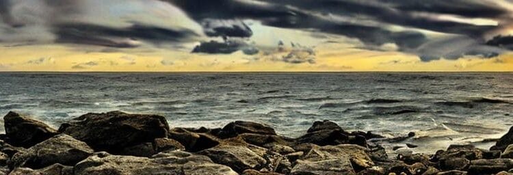 Creative creator's panoramic view of a rocky shoreline under a dramatic cloudy sky at sunset.